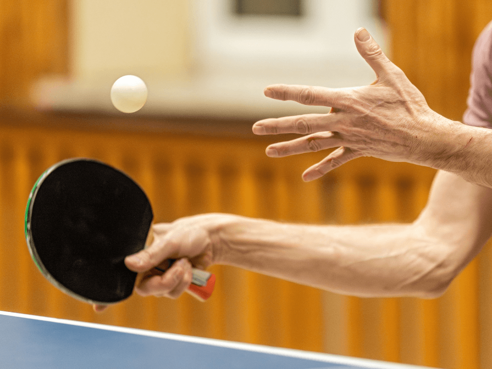 Jogador de tênis de mesa segura a raquete e posiciona a bola para o saque durante uma partida da modalidade esportiva. Tudo para explicar quanto ganha um jogador de tênis de mesa.